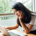 Woman working thoughtfully at laptop.